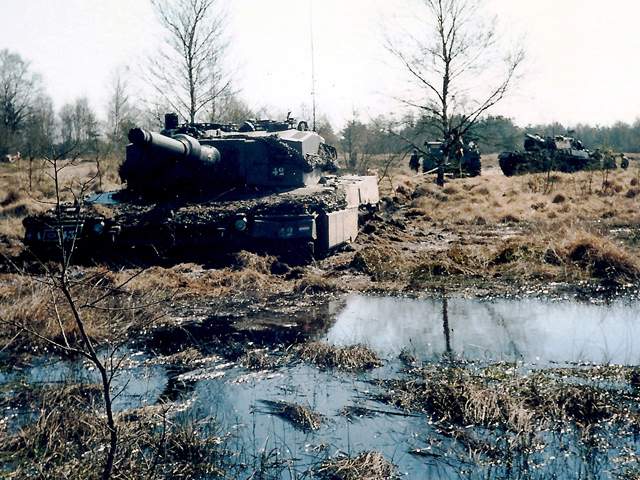 Een Leopard 2 tank vast in een Noord-Duits moeras met aan kabel naar een van twee andere tanks in de achtergrond.