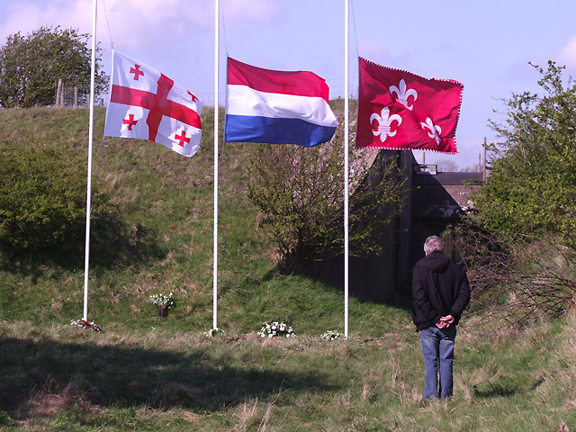 In rust overpeinzen bij de vlaggen en bloemen.