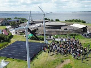 Luchtopname van de genodigden op het fort met de zonnepanelen en windmolens.