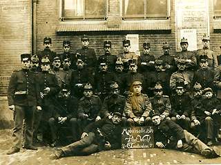 Groepsfoto van soldaten, gemaakt in oktober 1914, met enkele posters van de Volksuniversitet op de muur achter hen.